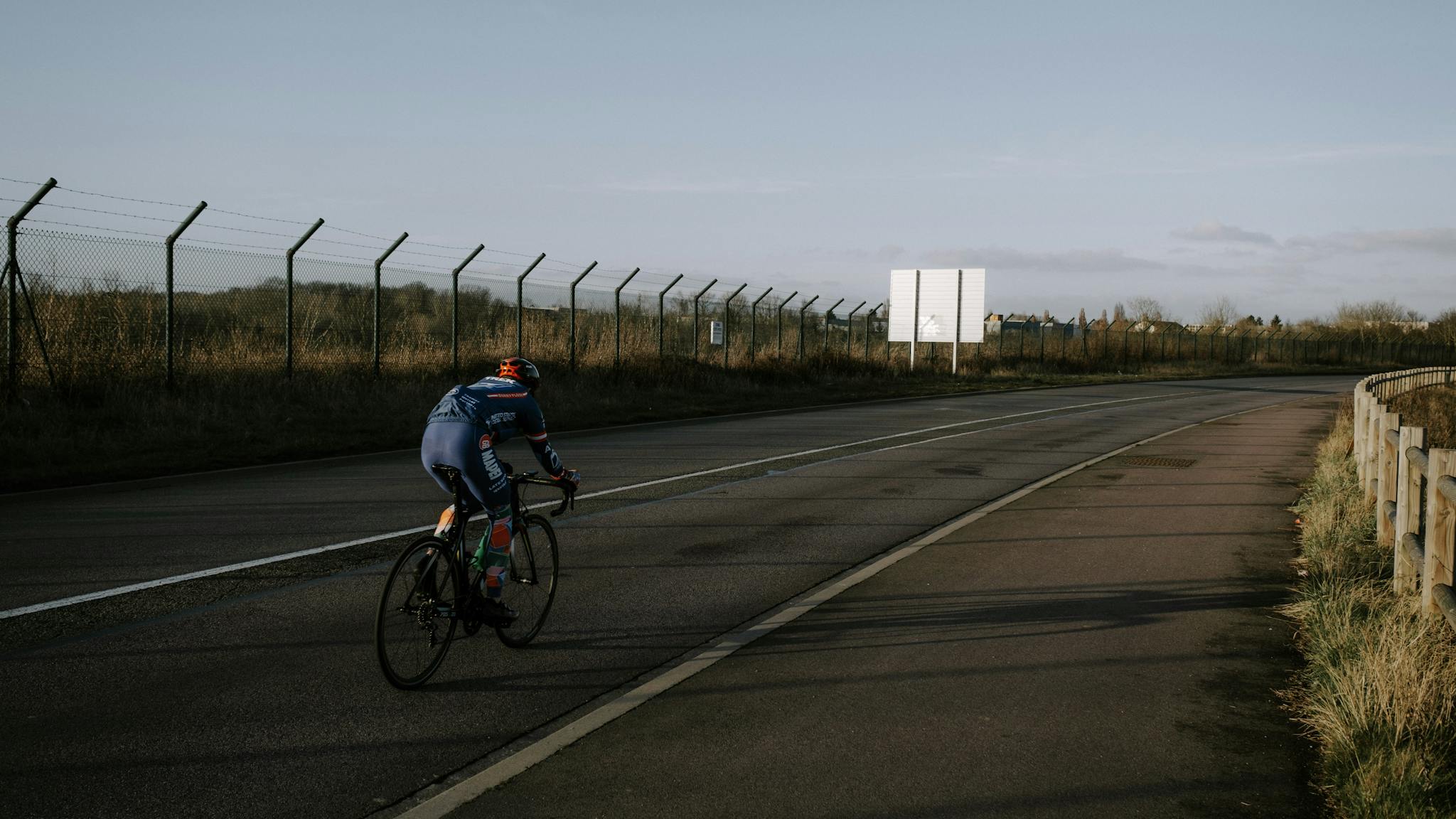 A cyclist rides along an empty road, showcasing a peaceful, outdoor biking scene.