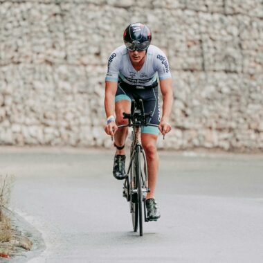 A male cyclist in full gear, riding on a road bike during an outdoor race.