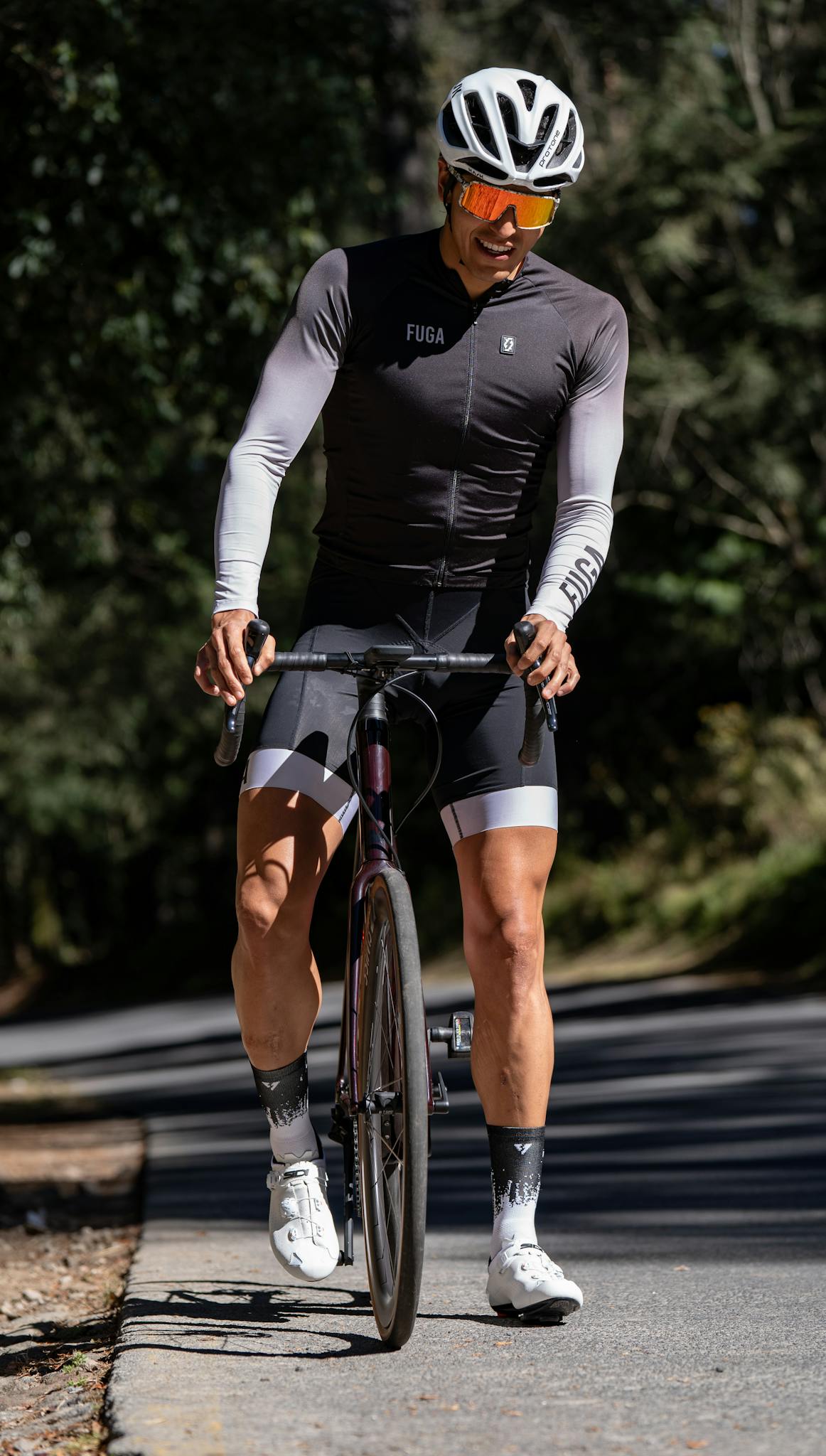 Male cyclist in professional gear riding through a scenic forest road during the day.
