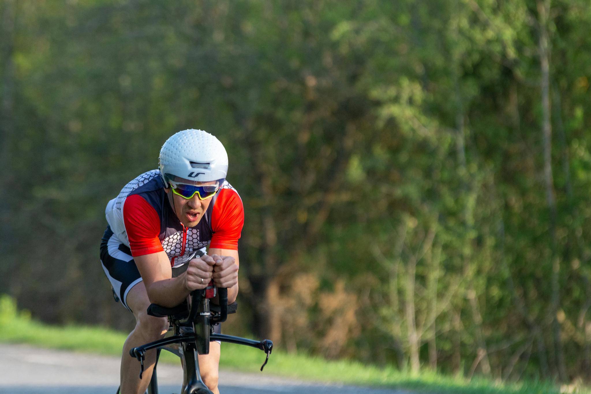 Triathlete cycling fast on a rural road during training, wearing a helmet and sunglasses.